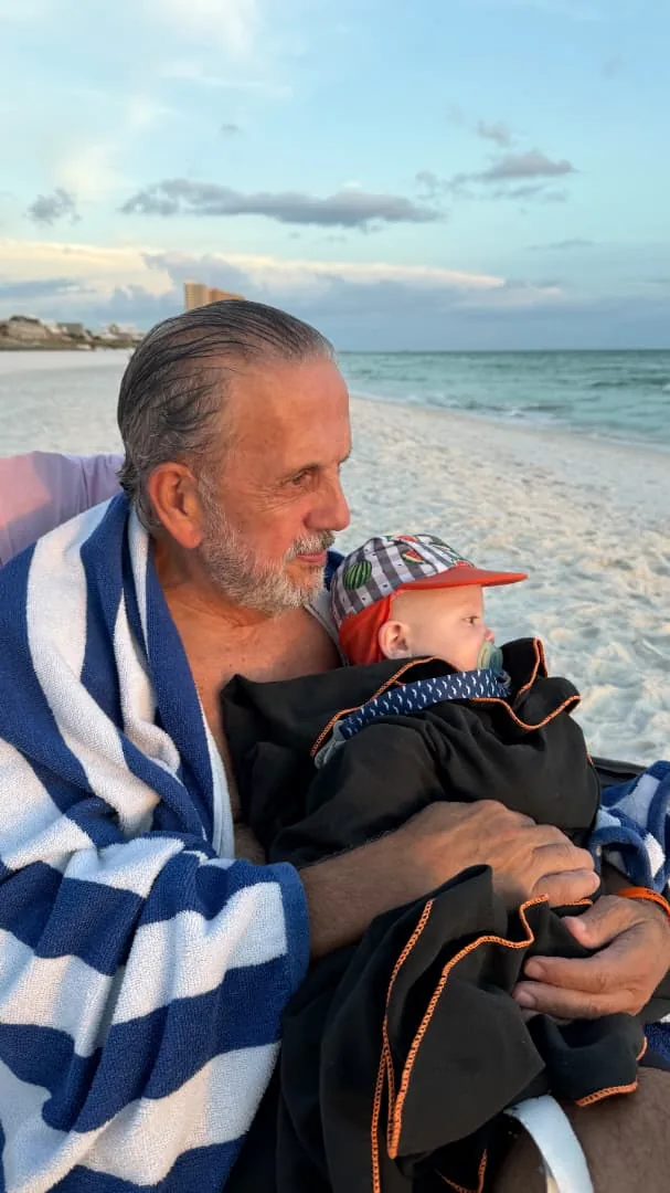 Eduardo Martí en la playa al atardecer, con su nieto recién nacido en brazos